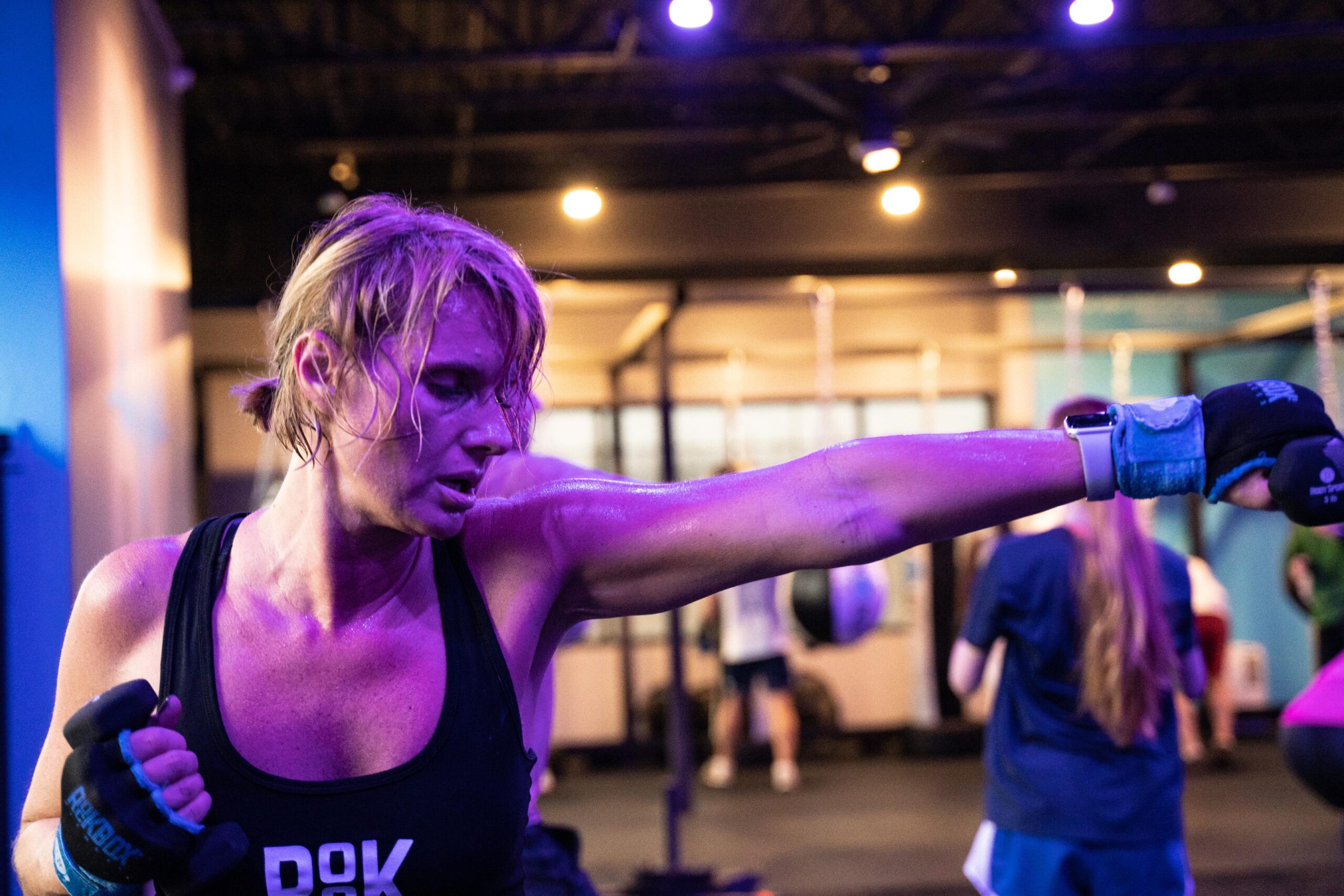 A female is shadow boxing with small weights on the strength side of the gym at a RockBox Fitness studio.